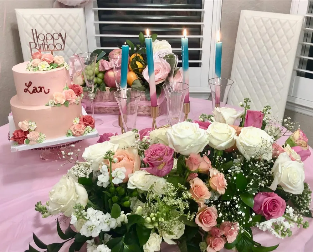 Lan’s two-tier pink cake on a party table beside a big centrepiece of white and pink roses and candles