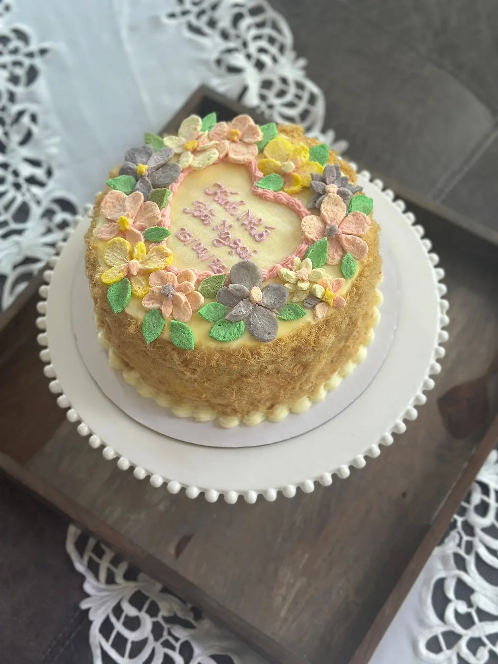 A salted egg sponge cake from above, ringed with pastel buttercream flowers around a handwritten message
