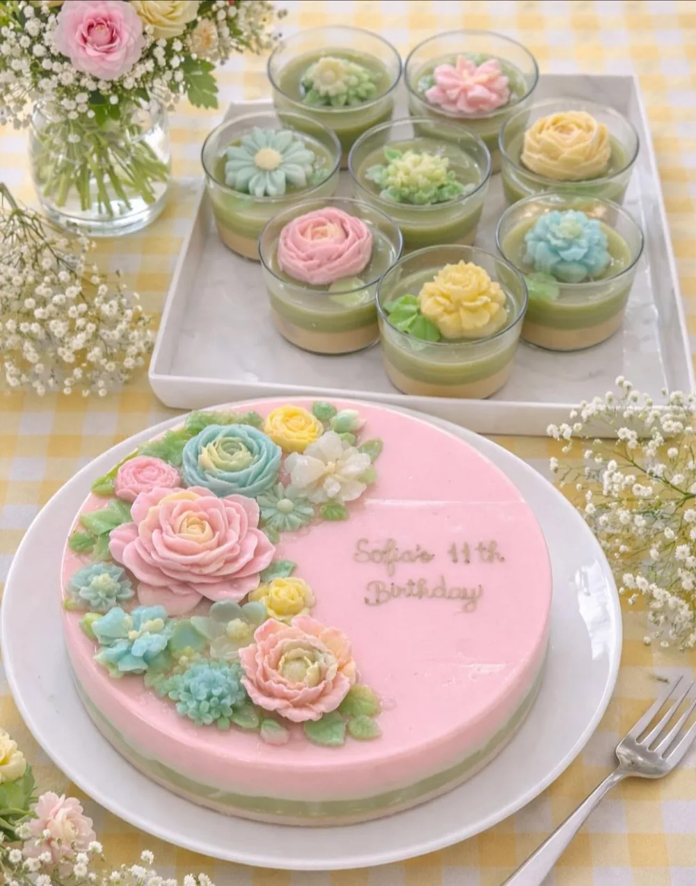 A pink jelly cake with blue, pink and cream jelly roses and “Sofia’s 11th Birthday”, with eight jelly flower cups behind it